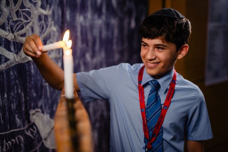 A JFS student lighting a Chanukah candle